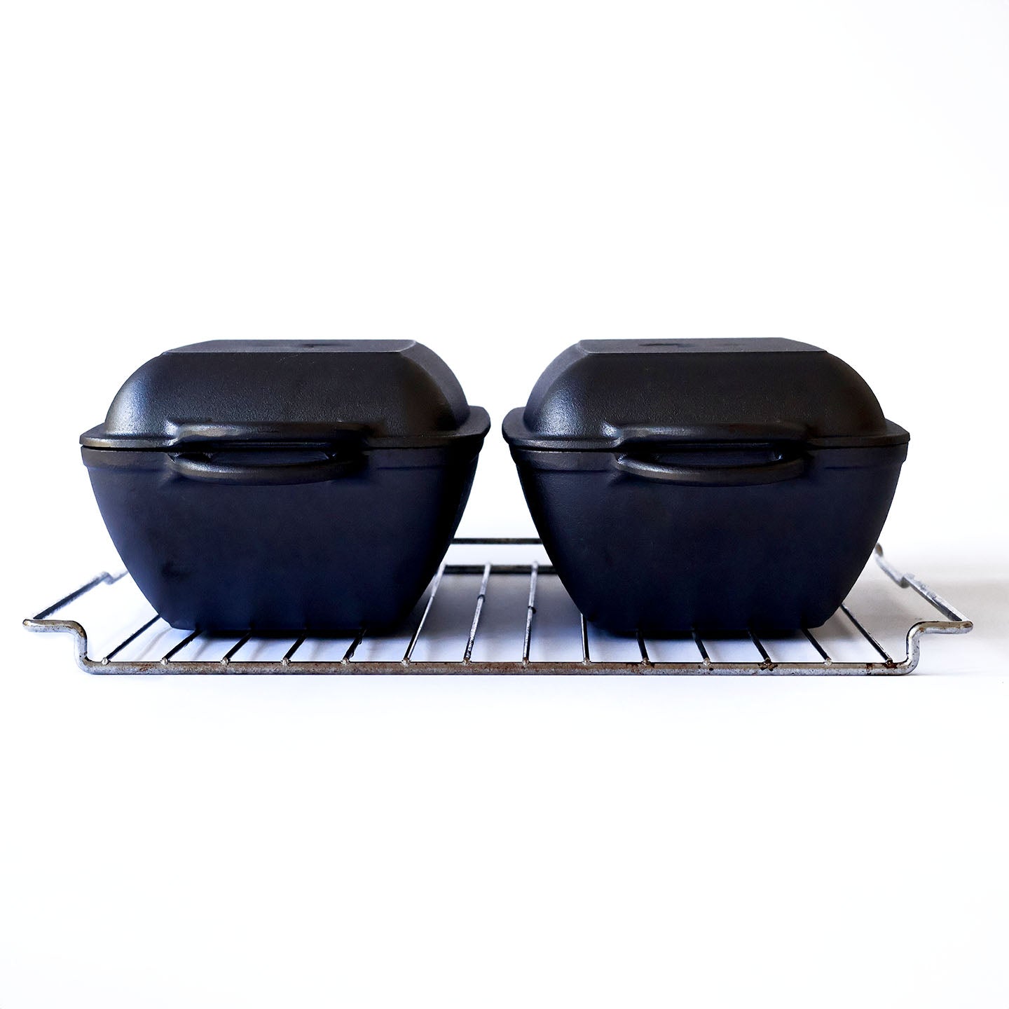 Two slim cast iron dutch ovens side by side on an oven tray, short-side view